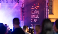 Publikum bei Konzert im Museumsinnenhof mit beleuchtetem Banner Kultur.findet.Stadt
