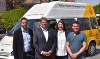 Vier Menschen stehen vor einem Auto und blicken zum Betrachter
