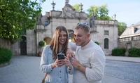 Zwei Menschen stehen vor einem barocken Tor und schauen auf ein Smartphone