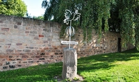 Eine Skulptur steht auf einer Wiese vor einer Mauer im Hintergrund