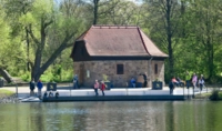 Ein kleines Haus mit Menschen davor von Wasser und Bäumen umgeben 