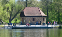 Ein kleines Haus mit Menschen davor von Wasser und Bäumen umgeben 