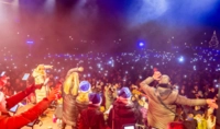 Viele Menschen stehen vor einer Bühne und halten eine Taschenlampe in die Luft