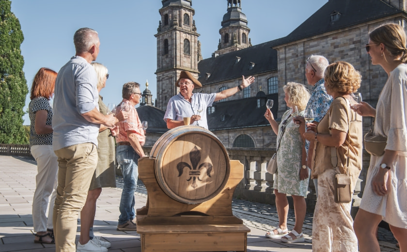 Menschen stehen um ein Fass herum, im Hintergrund ist der Fuldaer Dom zu sehen – Tourismus Fulda