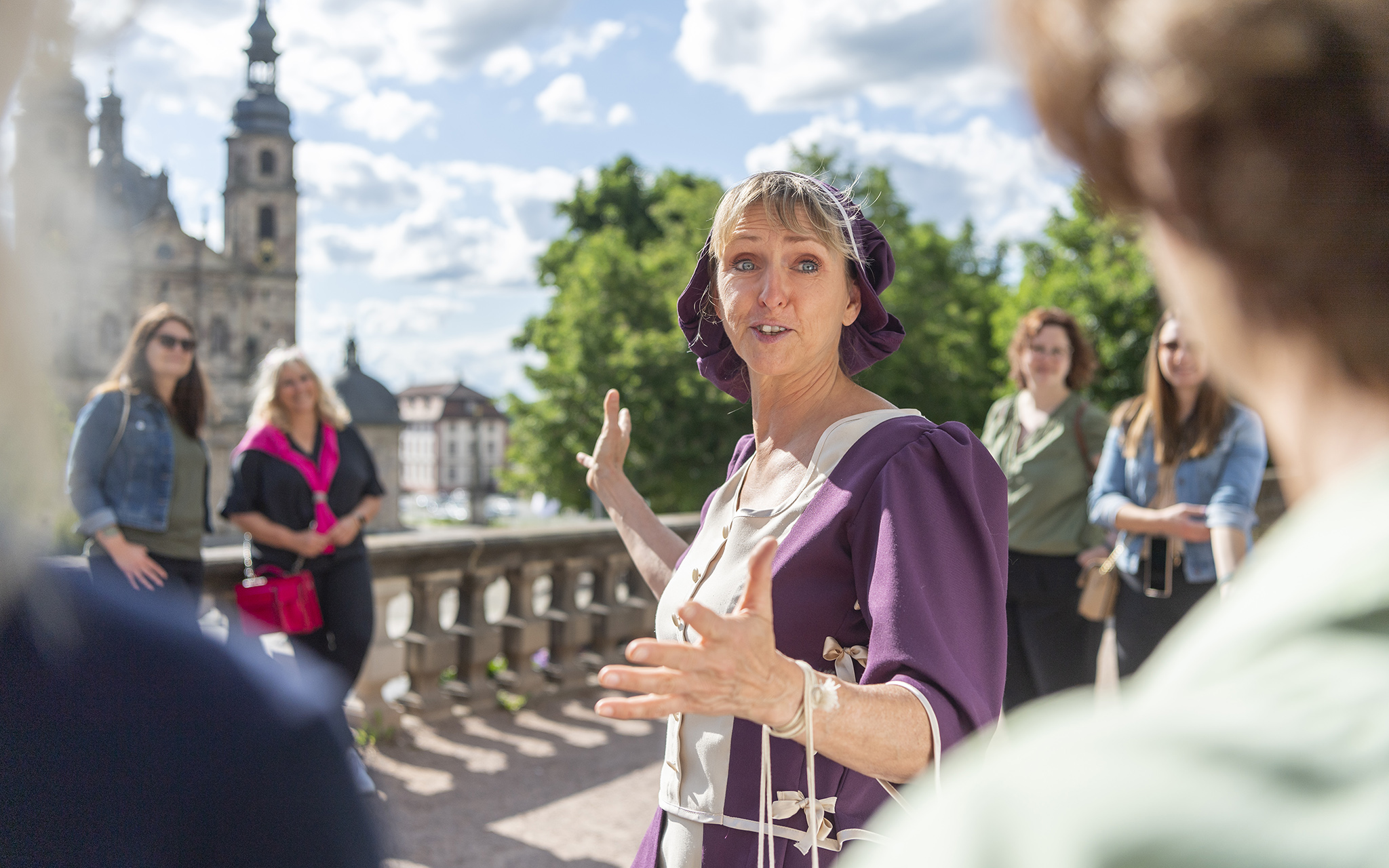 Eine Frau steht in traditioneller Kleidung aus dem 19. Jhd. vor einer Gruppe von Menschen